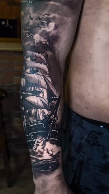 Tatuagem realista de veleiro em mar revolto no braço, black and gray por tatuador do Rio de Janeiro